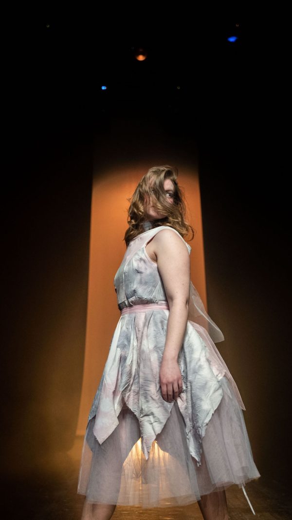 En elev iförd en elevdesignad klänning går på en catwalk.