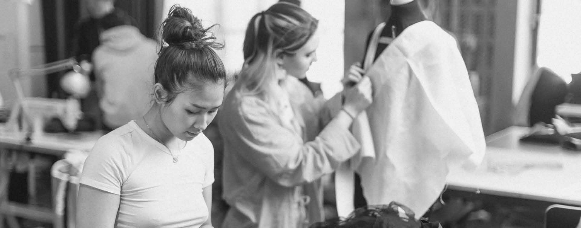 Elever arbetar fokuserat med kläder i verkstad, svartvitt.